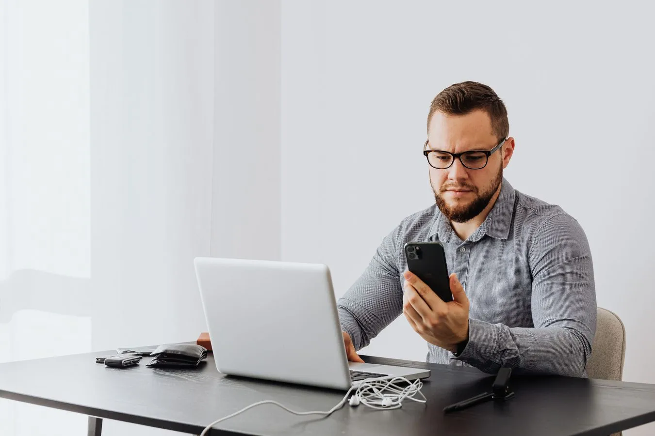 Business owner checking a smartphone at a desk beside a laptop