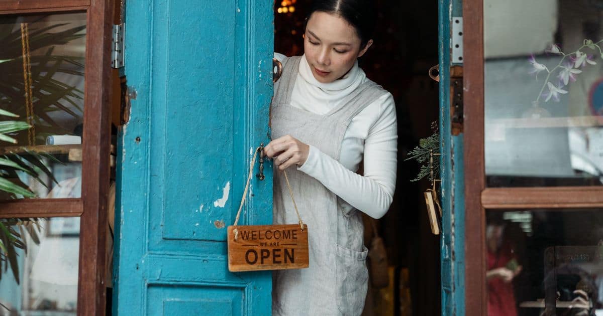 Shop owner hanging a wooden Welcome, Open sign on a blue shop door